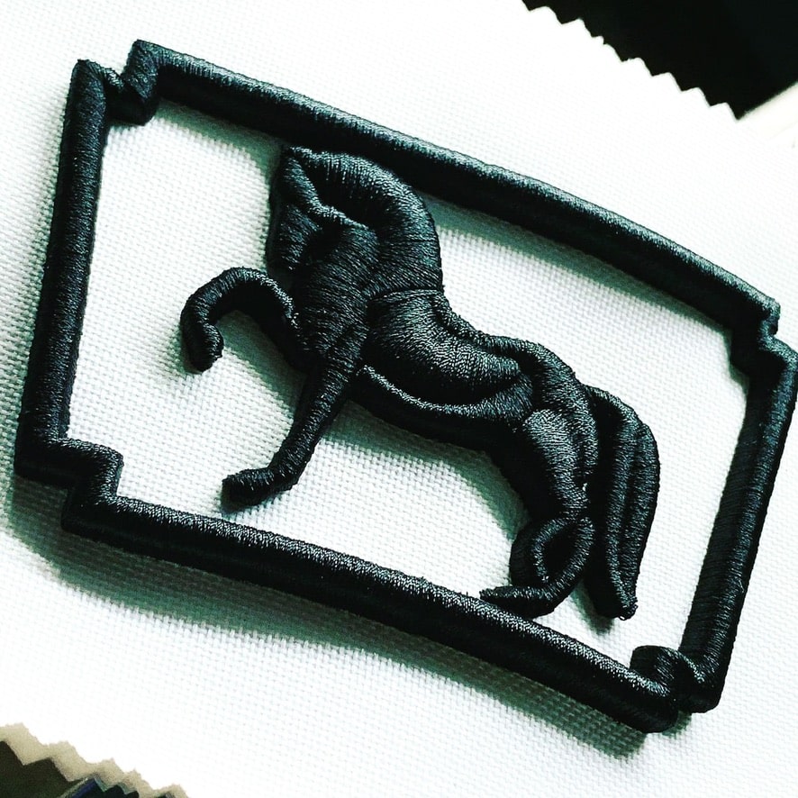 Motivo de caballo y marco bordado en relieve sobre tejido blanco.